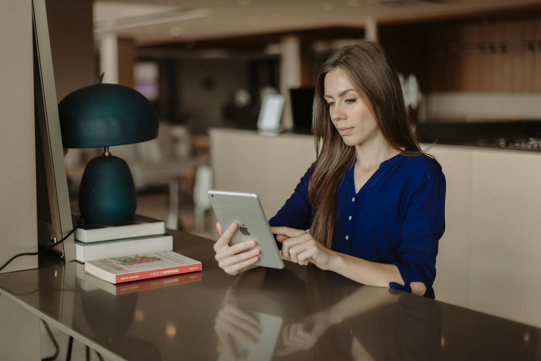 wordpress hotel booking plugin - Woman reading on a tablet at a desk with books in a modern office setting.