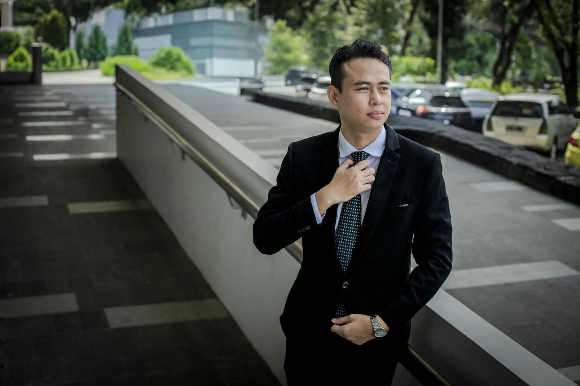cara menemukan keyword potensial - Confident young man in a suit adjusts his tie outdoors, exuding professionalism.