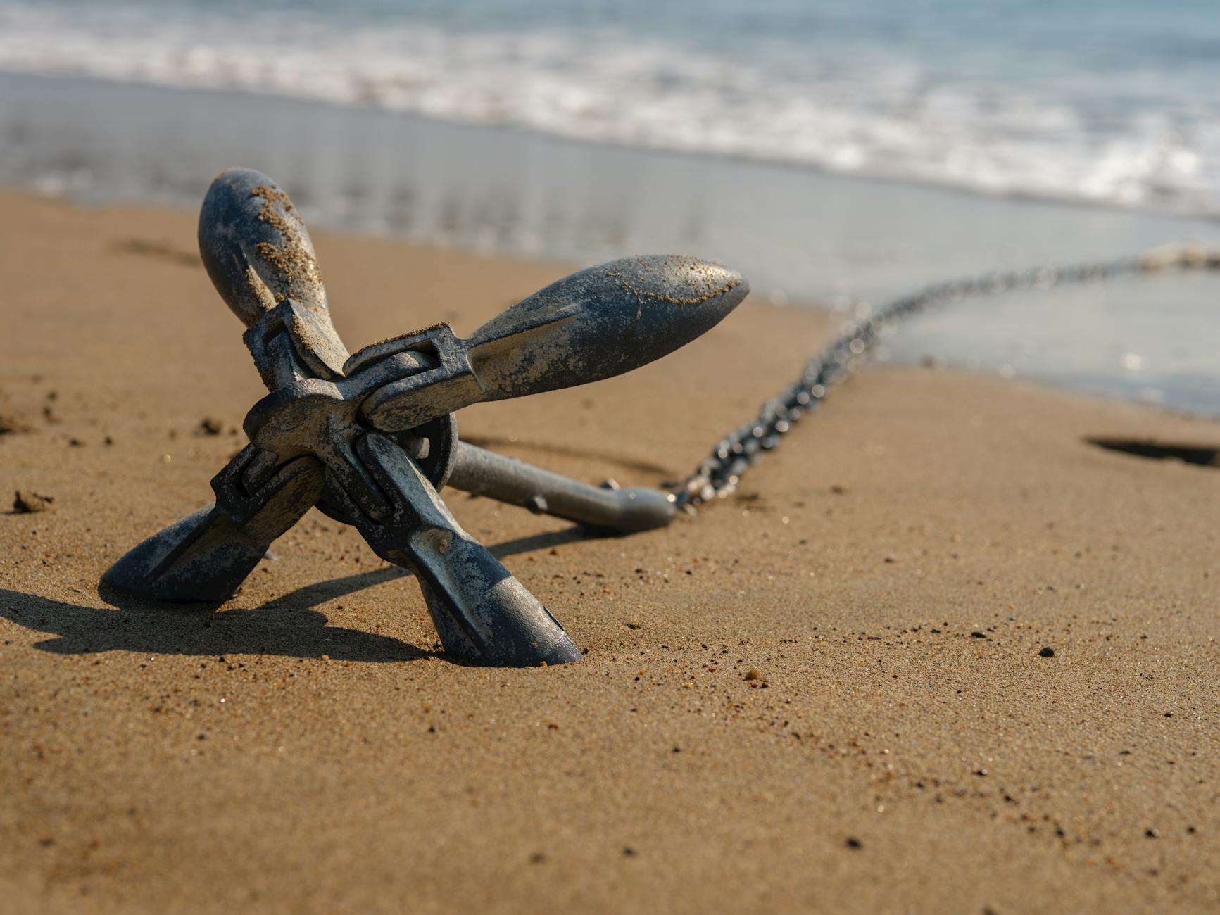 anchor text SEO - Close-up view of a metallic anchor resting on a sandy beach near the ocean shore.