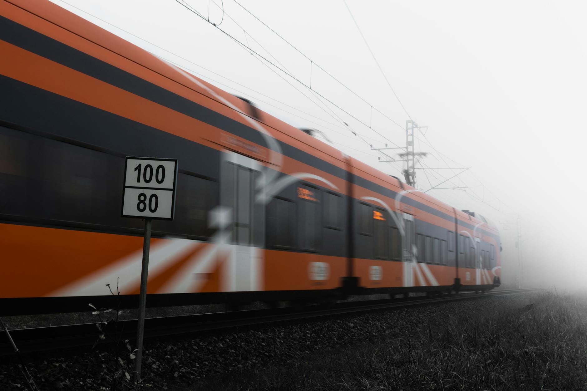 optimasi page speed - Orange train speeding on railway tracks in dense fog with speed sign visible.