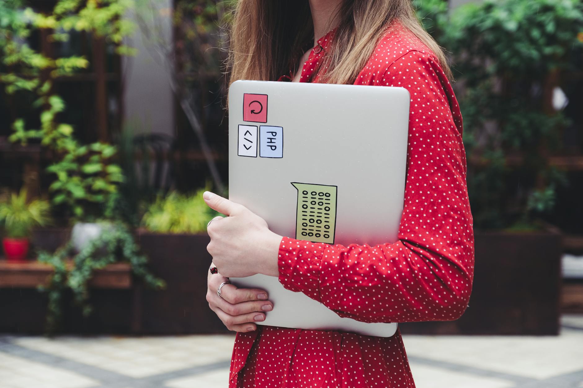 Core Web Vitals expertise - A young woman in a red polka dot shirt holds a laptop with stickers outdoors.