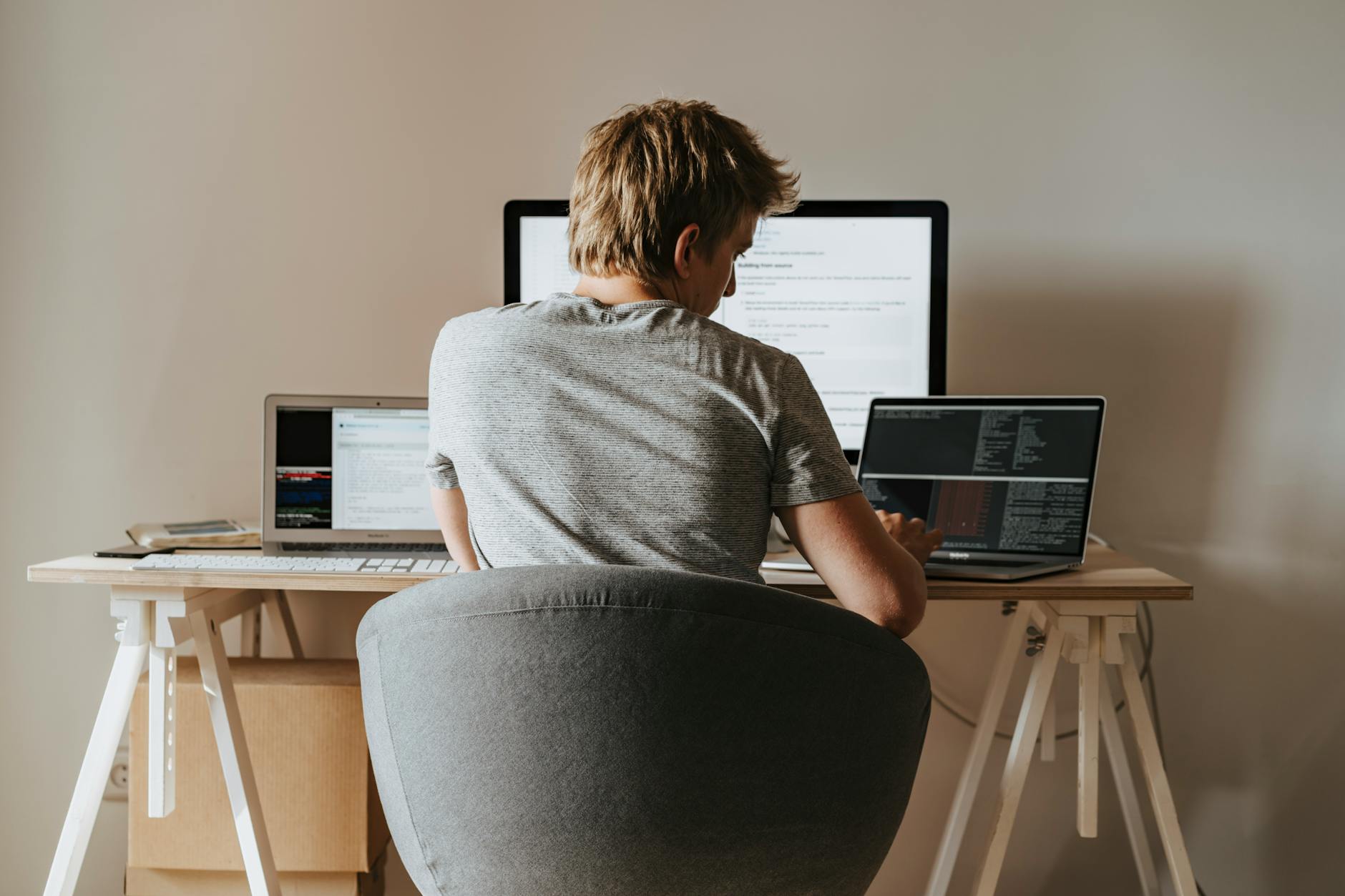 remote wordpress developer jobs - Young man coding at home office with multiple laptops, representing remote work and technology.