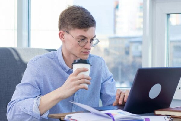 SEO specialist freelance - Adult wearing eyeglasses works remotely on a laptop while enjoying coffee indoors.