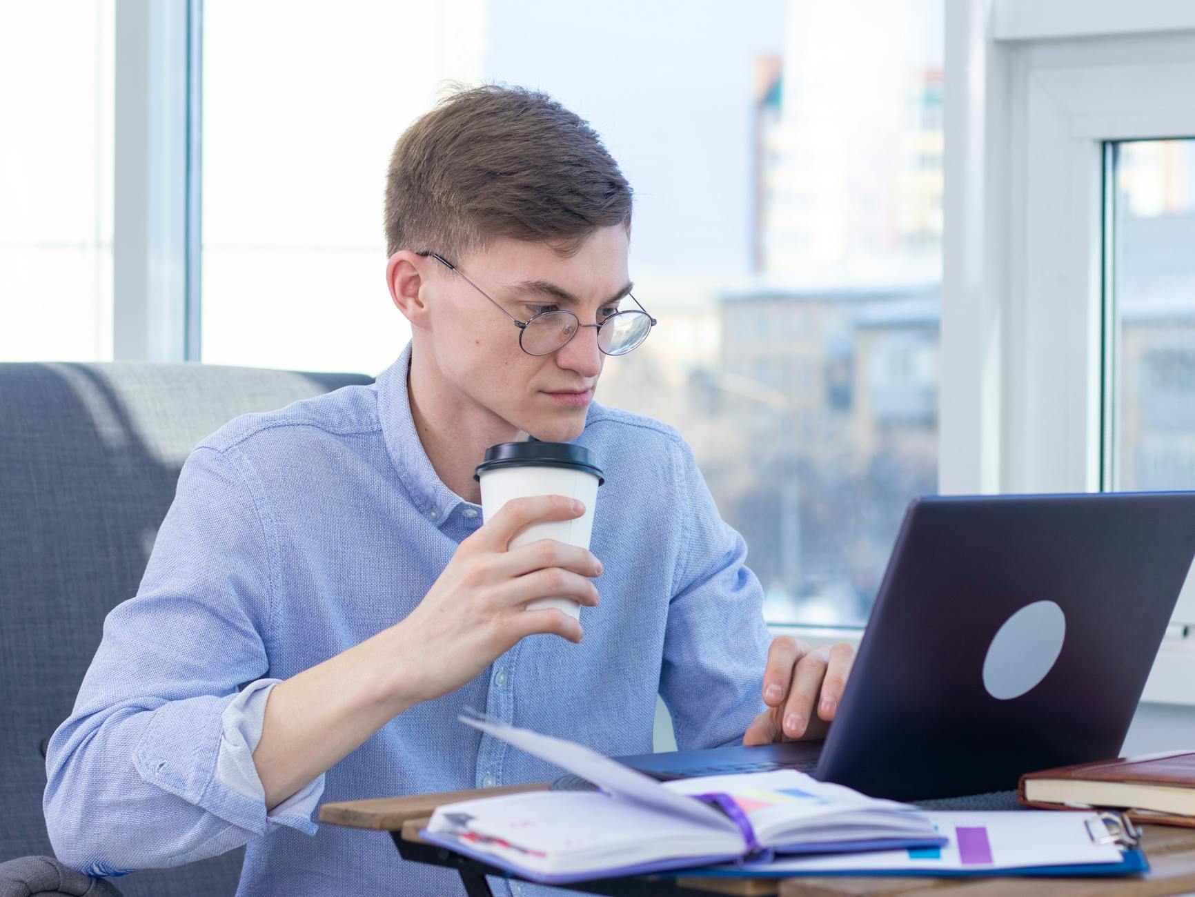 SEO specialist freelance - Adult wearing eyeglasses works remotely on a laptop while enjoying coffee indoors.