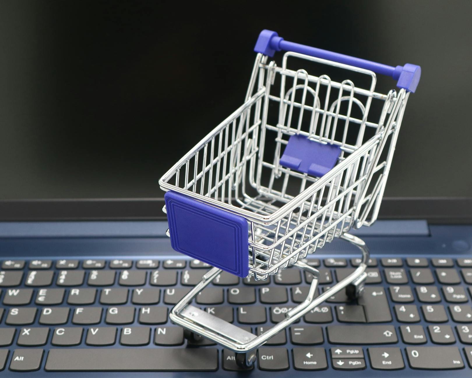 cara riset keyword e-commerce - A mini shopping cart placed on a laptop keyboard, symbolizing online shopping and digital retail.