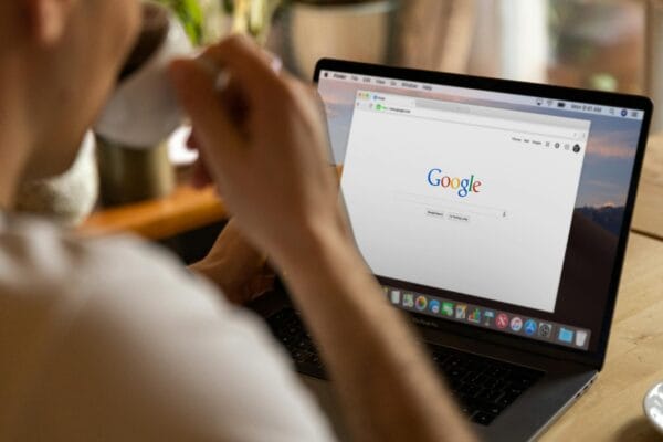 SEO dan Google Ads - Close-up of an adult drinking coffee and browsing Google on a laptop indoors.