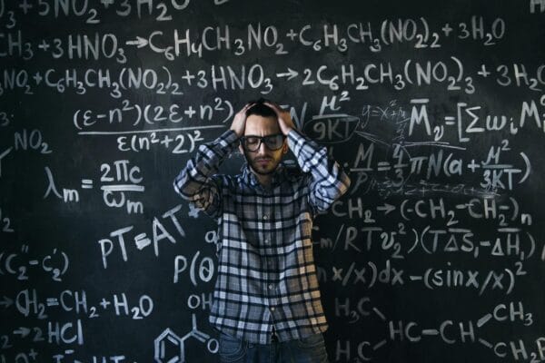 readability formula - Man in glasses focusing on math problems, struggling with complex equations on chalkboard.
