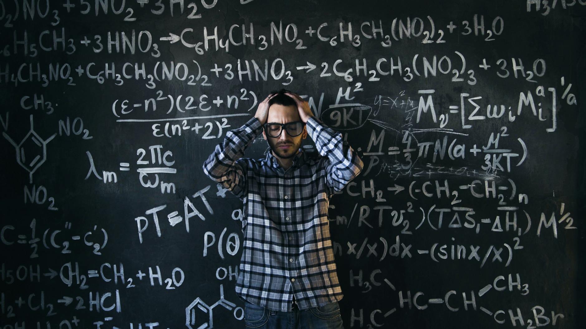 readability formula - Man in glasses focusing on math problems, struggling with complex equations on chalkboard.